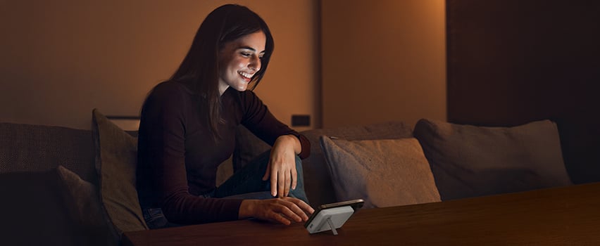 Kobieta uśmiecha się podczas bezprzewodowego ładowania smartfona powerbankiem Wozinsky na stole w przytulnym wieczornym świetle
